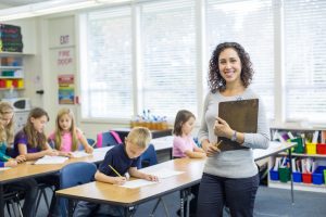 new teacher standing with book in front of her classroom