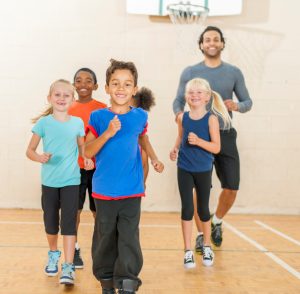 PE teacher jogging with group of young students