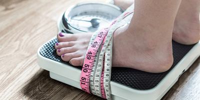 Woman standing on a scale with a measuring tape wrapped around her feet