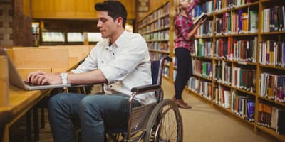 Student in wheelchair studying on computer at library