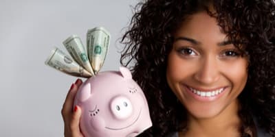 African American woman holding a piggy bank with money sticking out of it