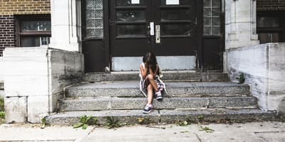 student sitting on stairs outside of school with her head in her hands