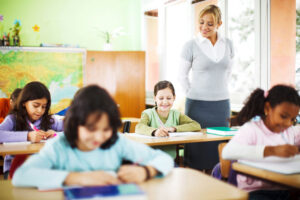 Young proud female teacher standing over student in full classroom
